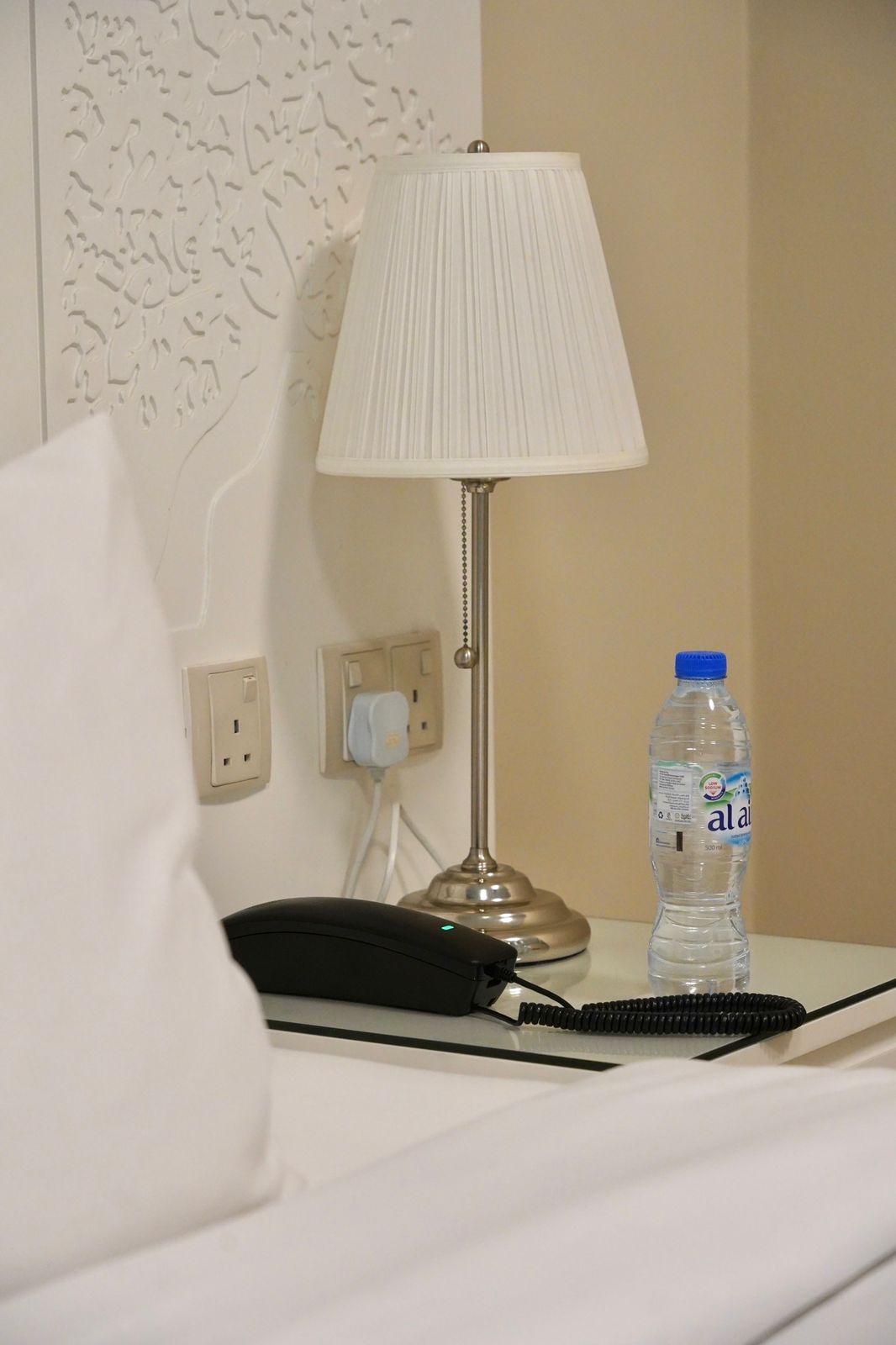 A Night Lamp Next to Bed with Water Bottle on The Nightstand
